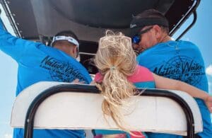 A group of people in blue shirts and one girl is sitting on the back of a boat.