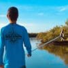 A boy standing on the shore of a lake holding a fishing rod.