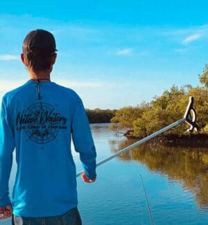 A boy standing on the shore of a lake holding a fishing rod.