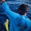 A man holding onto a yellow fish while standing in the ocean.