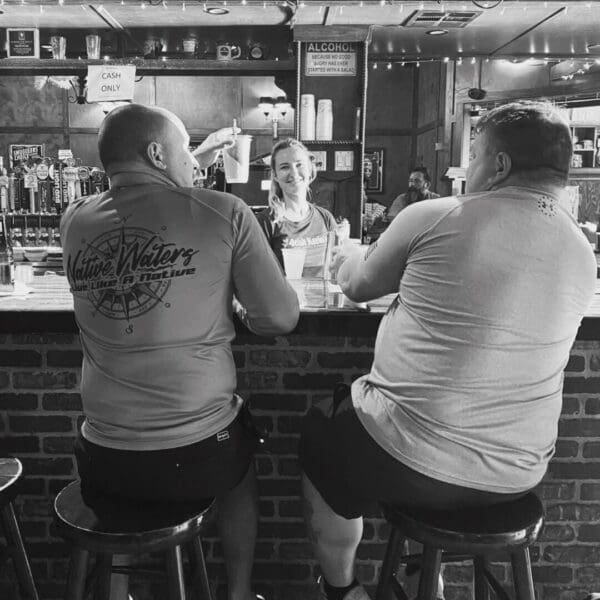 Two men sitting at a bar with one man looking on.